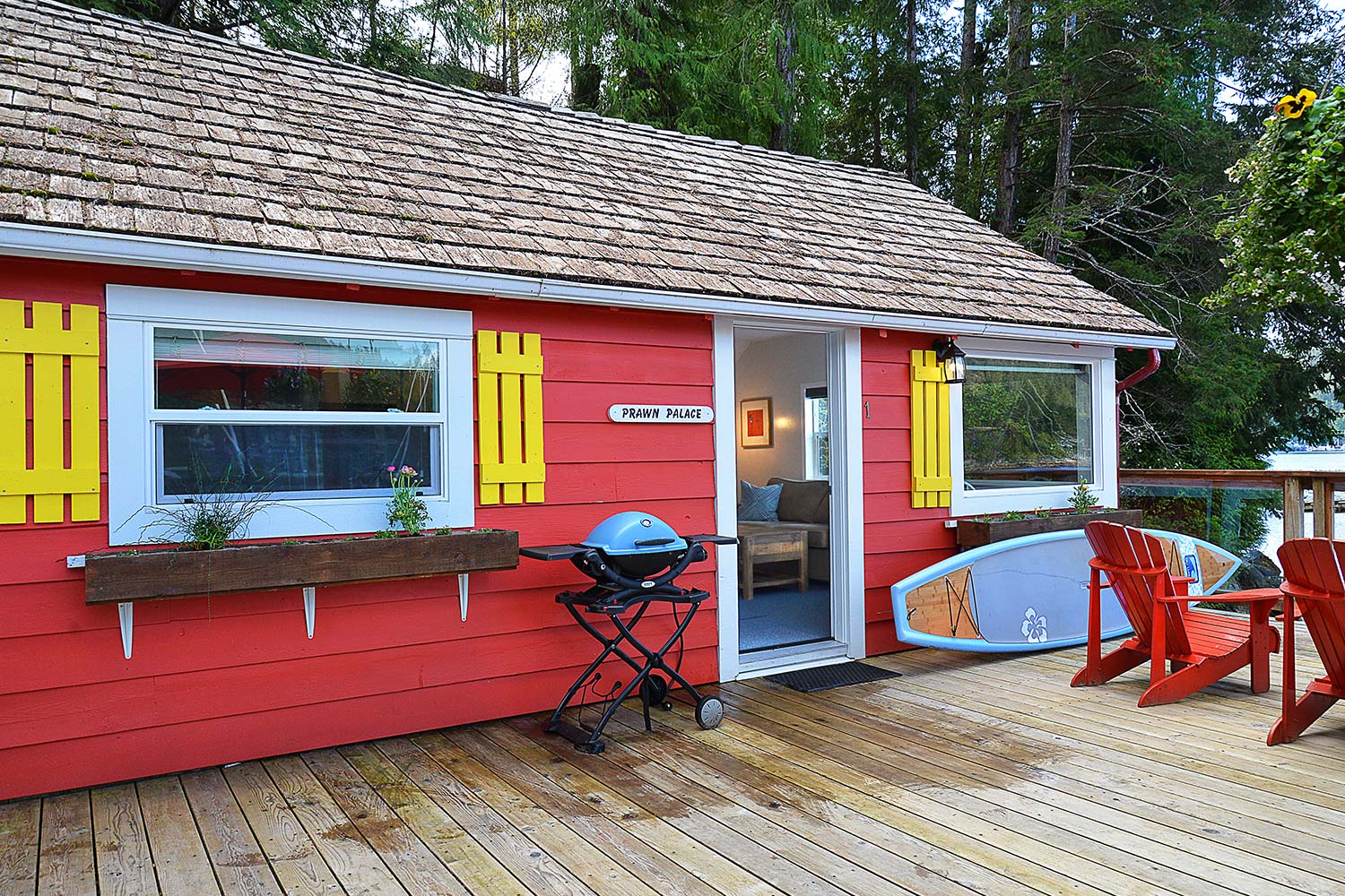 A Weber BBQ and stand-up paddleboard on the front deck of Prawn Palace. A cute cottage situated over the Pender Harbour.